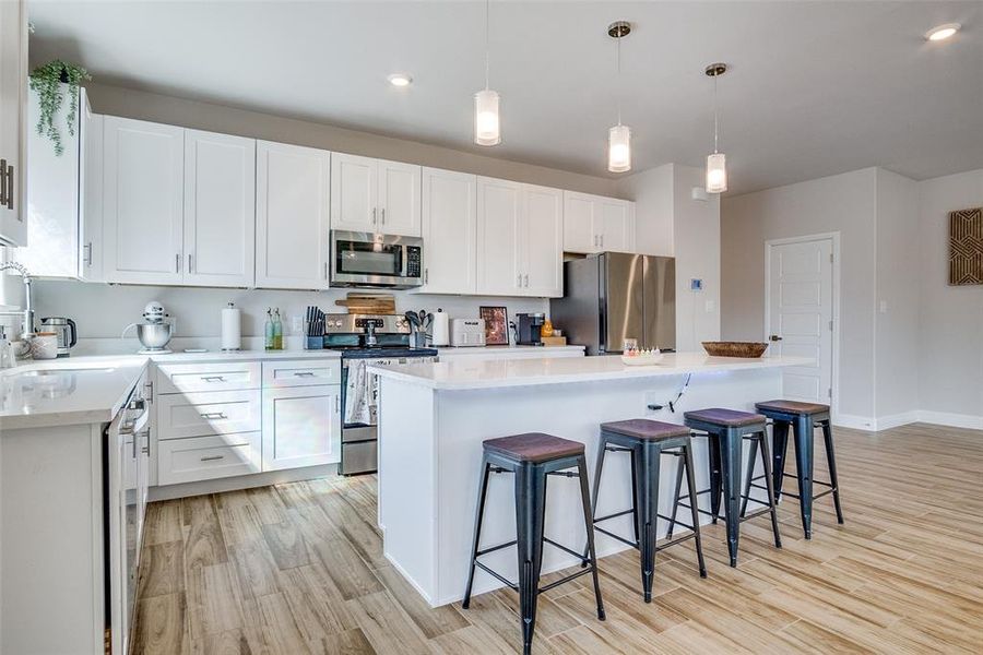 Kitchen with a kitchen island, a breakfast bar area, appliances with stainless steel finishes, hanging light fixtures, and white cabinets