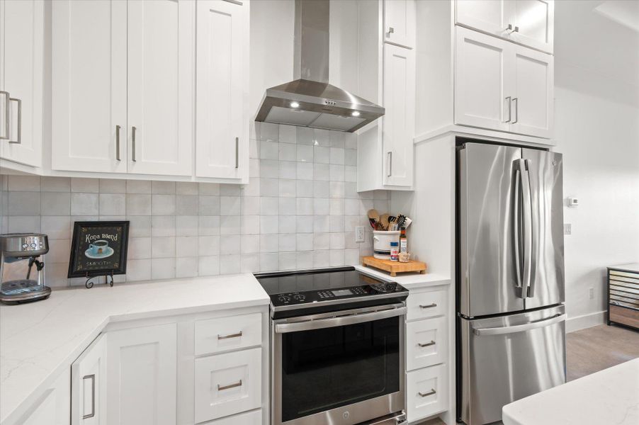 Kitchen featuring stainless steel appliances, white cabinets, light stone counters, and backsplash