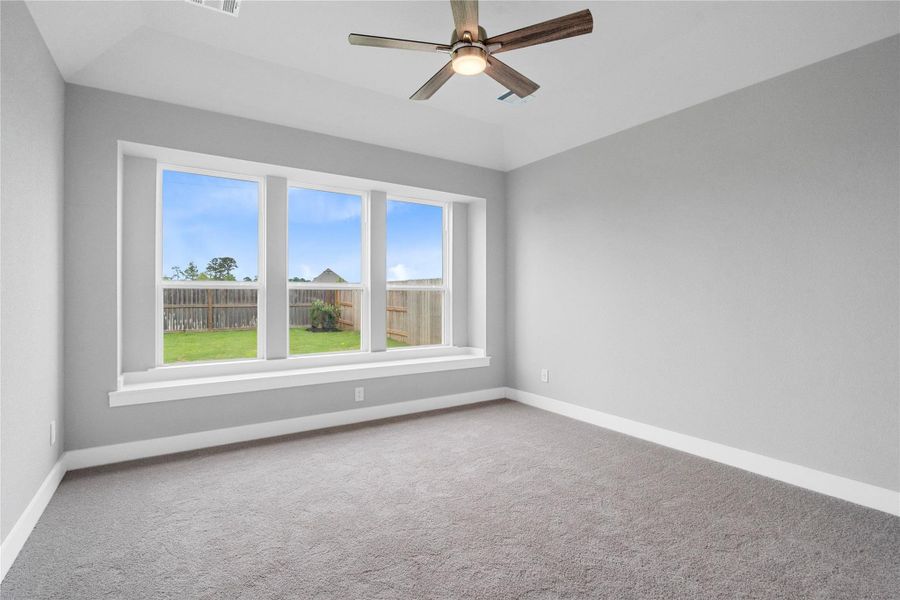 The primary bedroom provides a peaceful escape with a bright, neutral palette, sloped ceilings, ceiling fan, large windows with added window seat, and plush carpet flooring, creating a calm and restorative atmosphere to end your day.