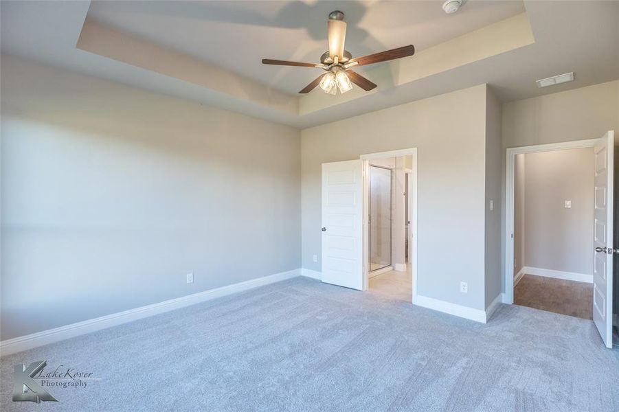 Unfurnished bedroom with a tray ceiling, light carpet, ceiling fan, and ensuite bath