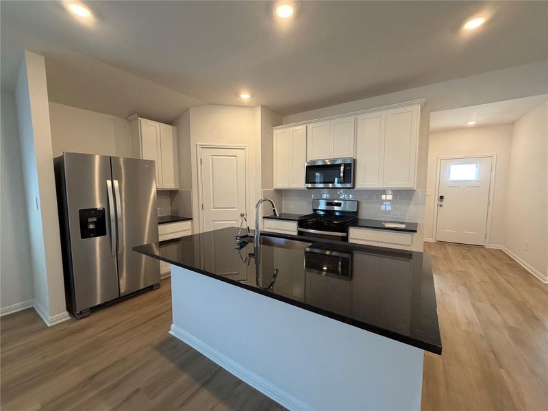 Kitchen featuring white cabinetry, appliances with stainless steel finishes, decorative backsplash, dark stone countertops, and light wood-type flooring