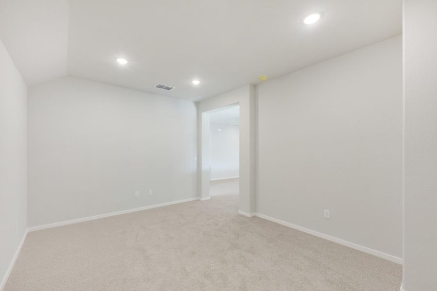 Empty bedroom with beige carpet, white walls, recessed lighting, and open doorway to adjoining room