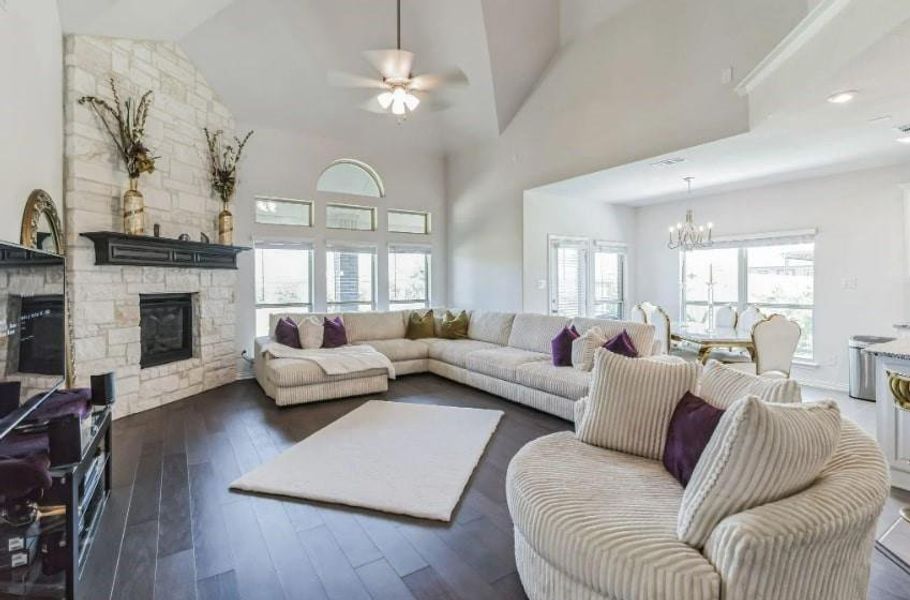 Living room featuring high vaulted ceiling, ceiling fan with notable chandelier, a fireplace, and dark hardwood / wood-style flooring