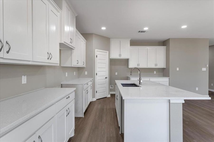 Kitchen with light stone counters, dark wood-style flooring, white cabinets, recessed lighting, and a center island with sink