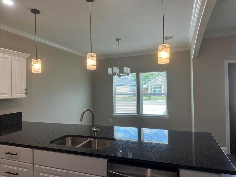 Kitchen with a sink, ornamental molding, dishwasher, white cabinets, and dark stone countertops