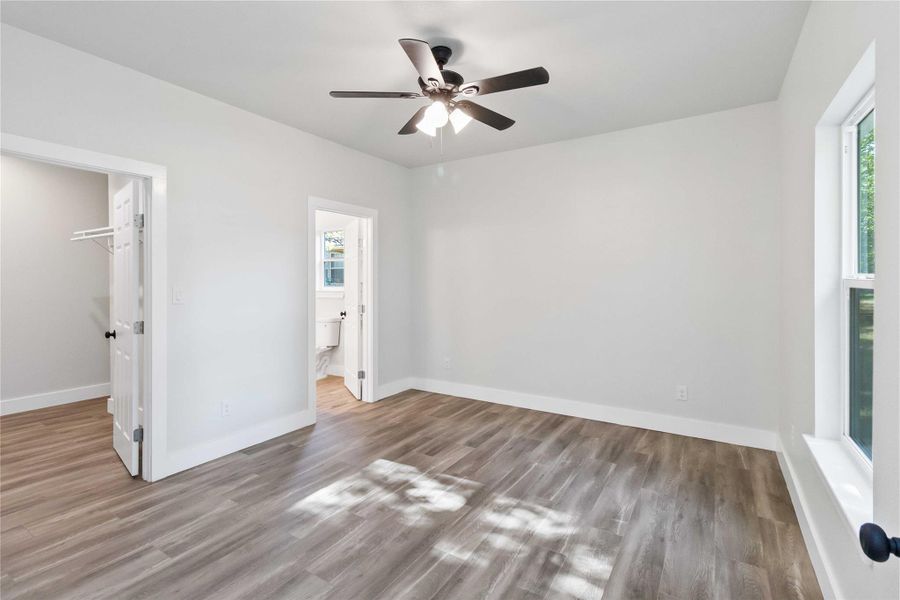 Unfurnished bedroom with a walk in closet, light wood-type flooring, a ceiling fan, and connected bathroom