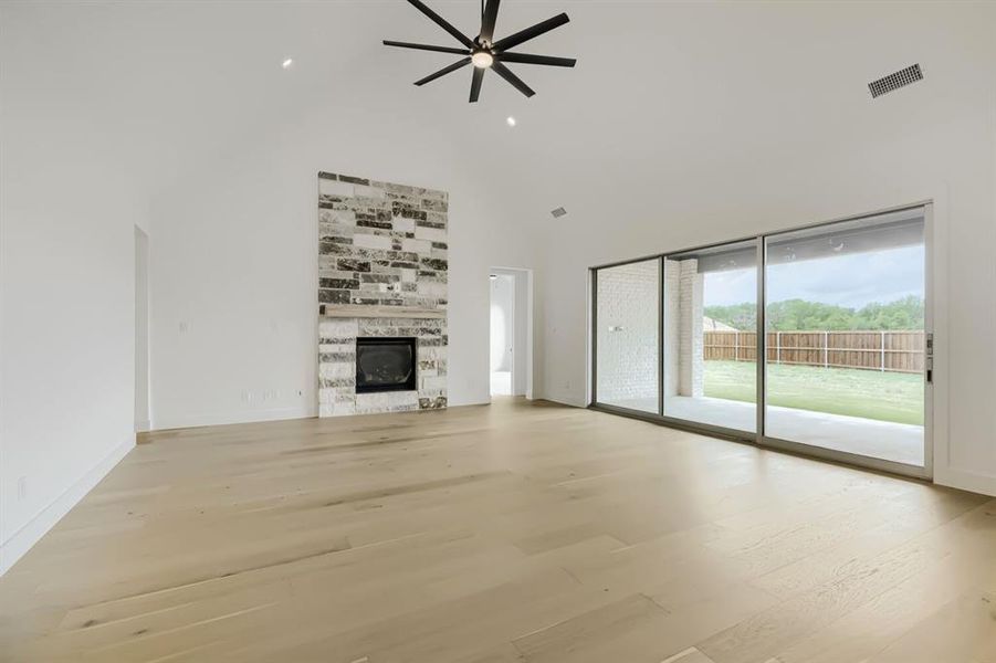 Unfurnished living room featuring a glass covered fireplace, ceiling fan, a high ceiling, light wood-style floors, and recessed lighting