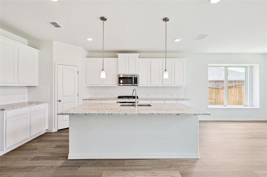 Kitchen featuring sink, light stone counters, light hardwood / wood-style floors, a kitchen island with sink, and white cabinets