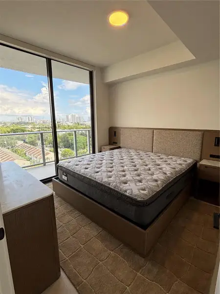 Floor-to-ceiling glass sliding doors, private balcony with metal railing, built-in wooden headboard with integrated lighting and electrical outlets, recessed ceiling lighting, and solid-surface topped wooden cabinetry Floor-to-ceiling glass sliding doors, private balcony with metal railing, built-in wooden headboard with integrated lighting and electrical outlets, recessed ceiling lighting, and solid-surface topped wooden cabinetry