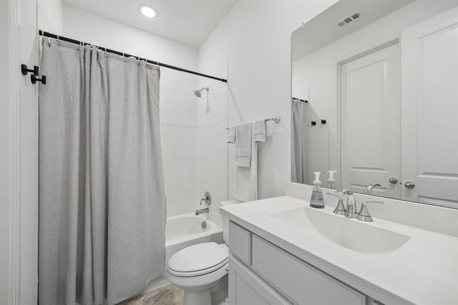 Bathroom featuring a white subway tile shower, a chrome showerhead with matching fixtures, a white toilet, a single vanity with a white countertop, and a large wall-mounted mirror