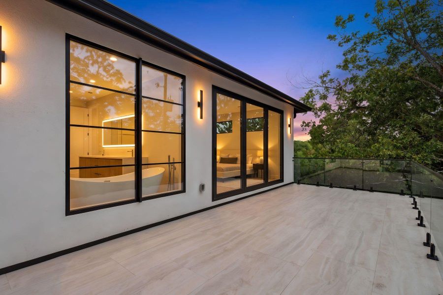 Tiled flooring and glass railings define this upper-level terrace overlooking mature trees.