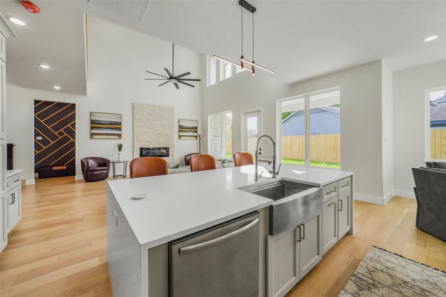 This modern home features an open-concept living area with high ceilings, a sleek kitchen island with a farmhouse sink, stainless steel appliances, and abundant natural light from large windows. The living room has a contemporary fireplace and stylish finishes, offering a spacious and inviting atmosphere.