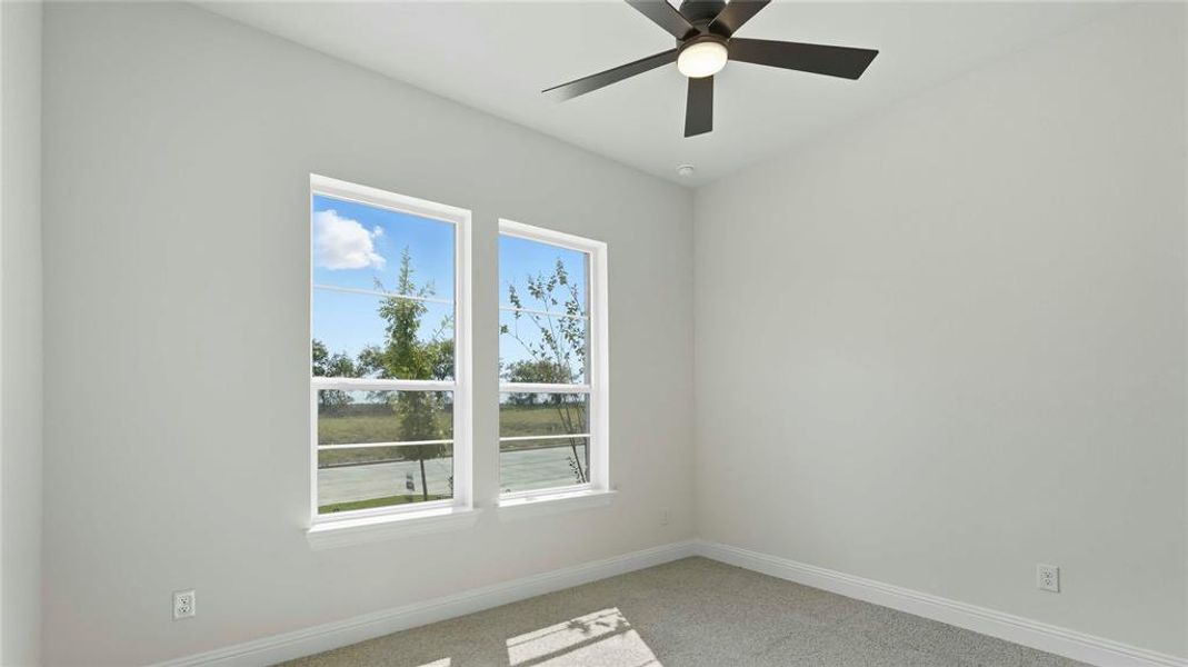 Room featuring two double-hung windows with white trim, a dark-toned ceiling fan with integrated lighting, light gray wall paint, and gray carpeted flooring