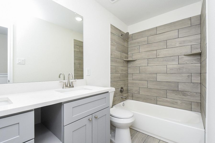 This is a modern bathroom featuring a sleek gray vanity with ample counter space and storage, a large mirror, a white integrated sink with a brushed nickel faucet, and a built-in bathtub with wood-look tile surround. The space is well-lit and has a clean, contemporary design. This is a modern bathroom featuring a sleek gray vanity with ample counter space and storage, a large mirror, a white integrated sink with a brushed nickel faucet, and a built-in bathtub with wood-look tile surround. The space is well-lit and has a clean, contemporary design.