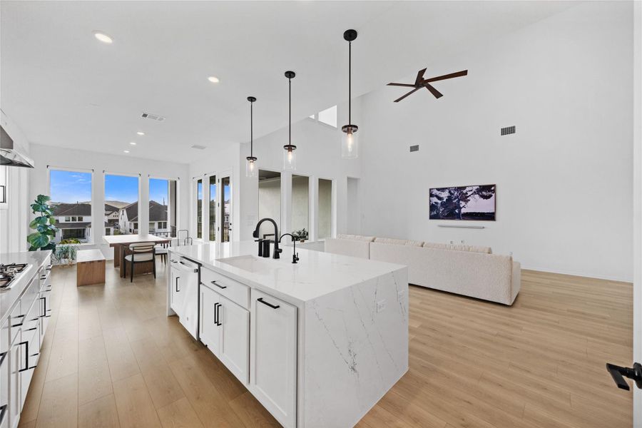 Kitchen with white cabinetry, decorative light fixtures, light stone countertops, light wood finished floors, and open floor plan