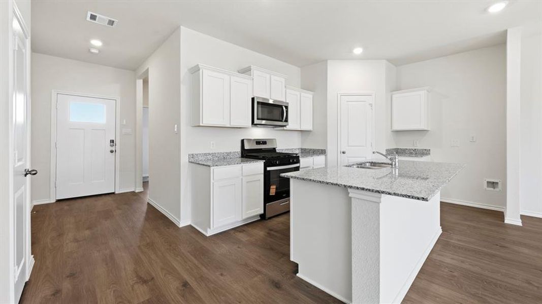 Kitchen with stainless steel appliances, white cabinets, light stone countertops, a center island with sink, and dark wood-style floors