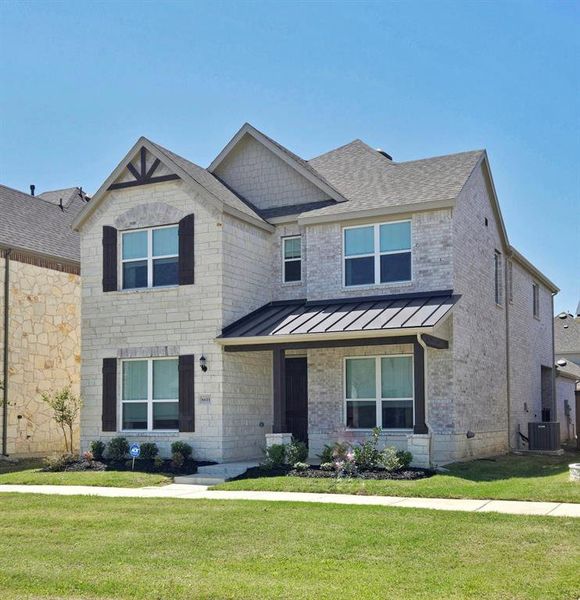 View of front of home featuring a front yard, metal roof, cooling unit, brick siding, and a standing seam roof