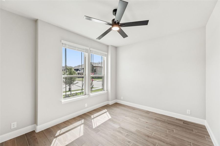 Empty bedroom with light wood floors, ceiling fan, and two windows with neighborhood view