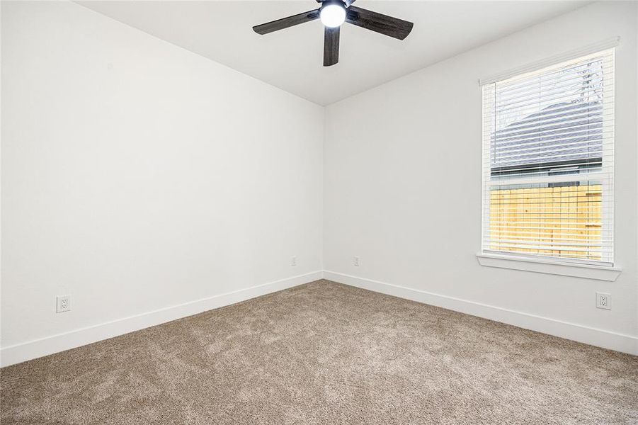 This room features neutral carpeting, white walls, and a ceiling fan with light. A large window with blinds provides natural light, creating a bright and airy space.