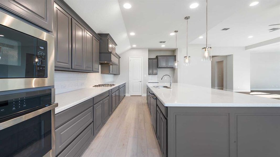 Kitchen with pendant lighting, a large island with sink, sink, light hardwood / wood-style floors, and stainless steel appliances