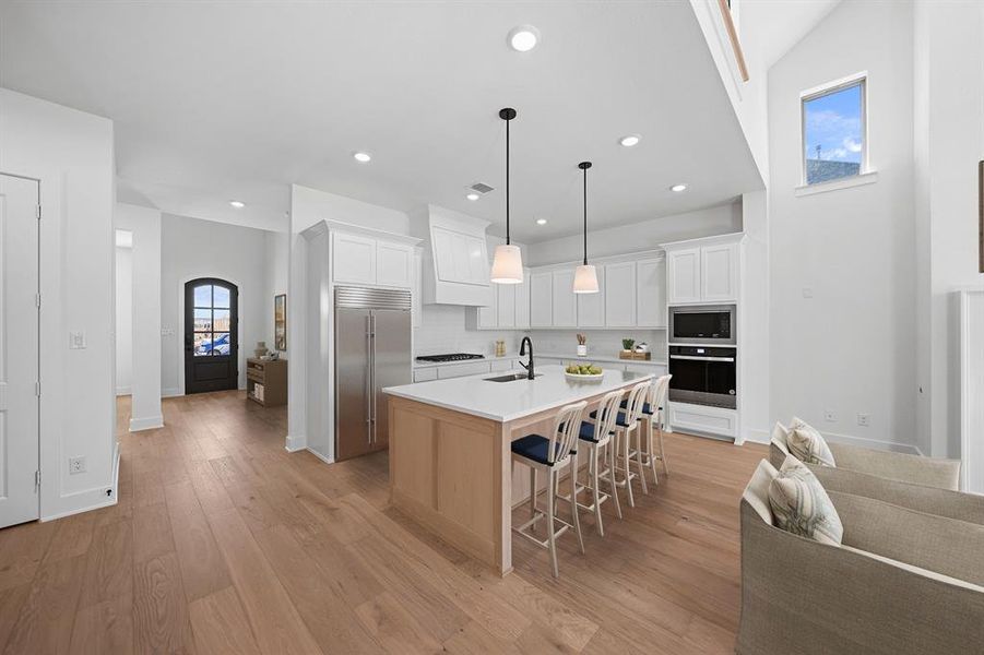 Kitchen featuring white cabinets, a breakfast bar, built in appliances, arched walkways, and light wood-style floors