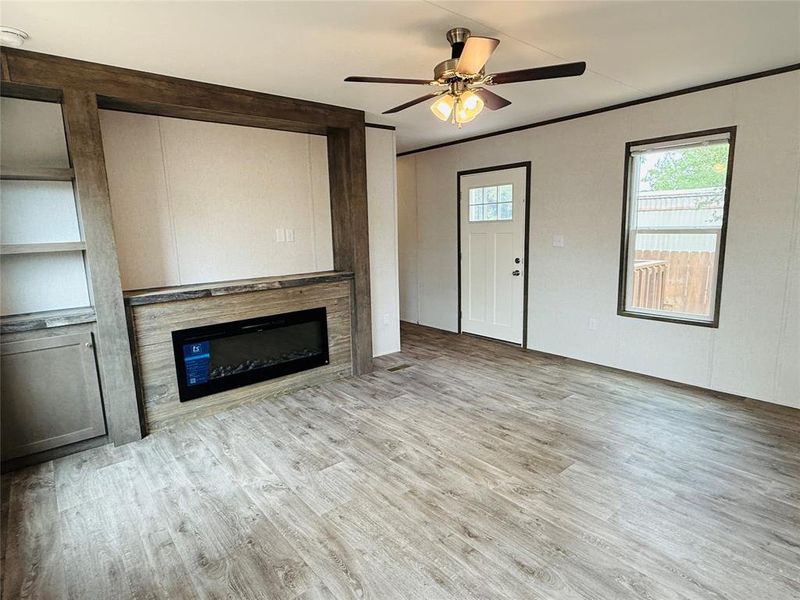 Unfurnished living room featuring a glass covered fireplace, wood finished floors, and a ceiling fan