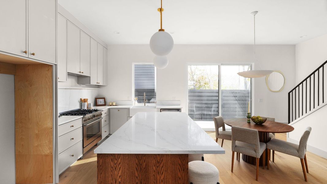 Kitchen with white cabinets, light stone countertops, high end stove, and light wood-style floors