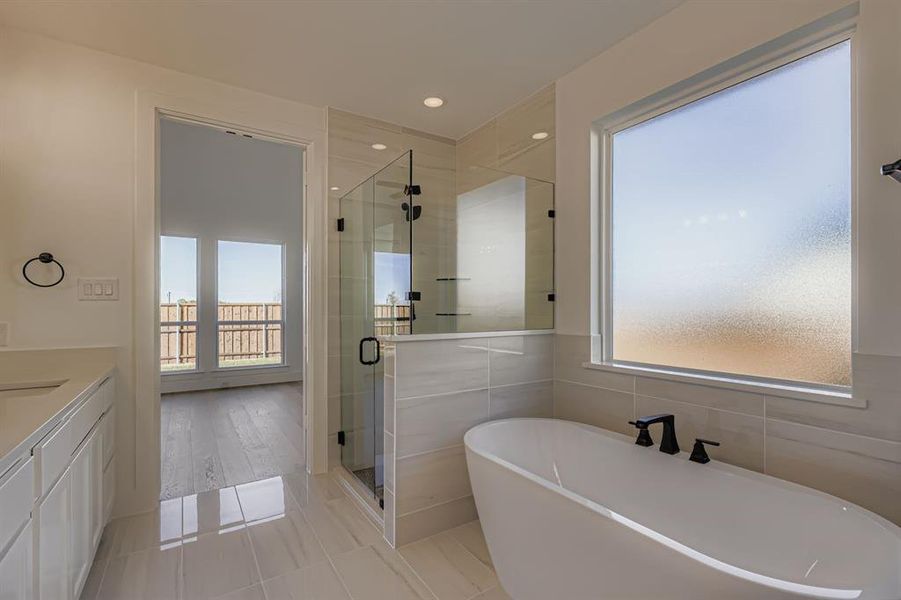 Full bathroom with a freestanding bath, vanity, a shower stall, light tile patterned flooring, and tile walls Full bathroom with a freestanding bath, vanity, a shower stall, light tile patterned flooring, and tile walls