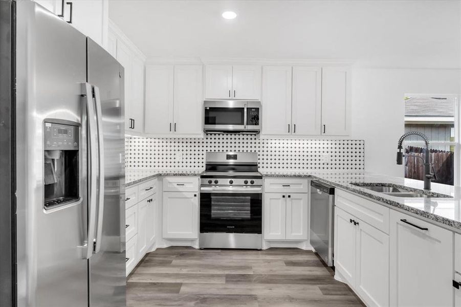 Kitchen featuring appliances with stainless steel finishes, sink, light stone counters, and white cabinets