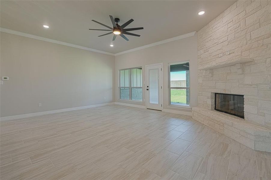 Unfurnished living room featuring ornamental molding, a stone fireplace, recessed lighting, wood tiled floors, and ceiling fan