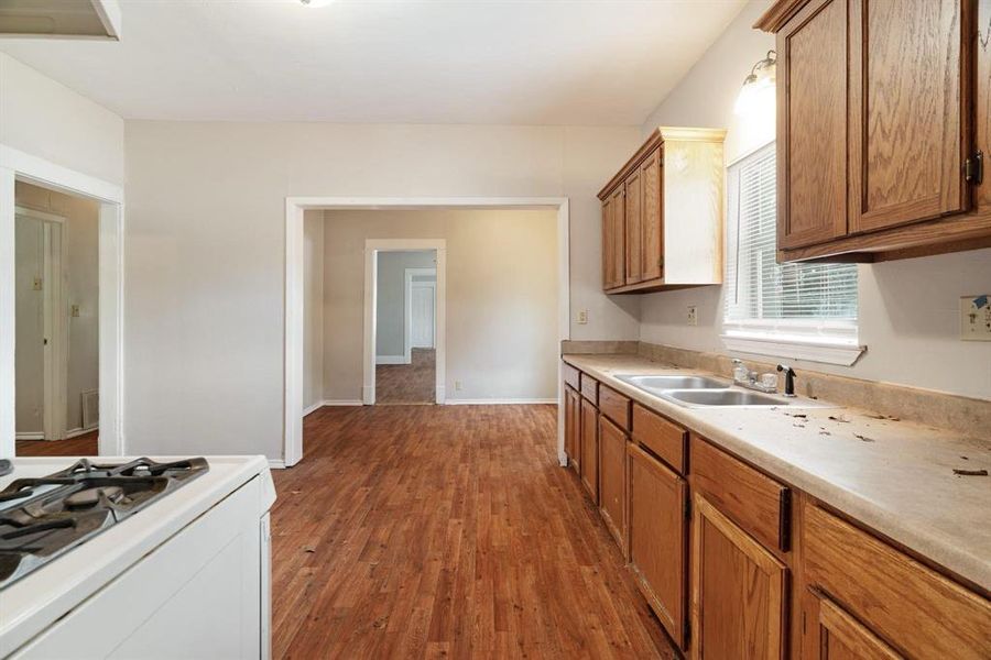 Kitchen featuring white range with gas stovetop, dark wood-style floors, brown cabinets, and light countertops Kitchen featuring white range with gas stovetop, dark wood-style floors, brown cabinets, and light countertops