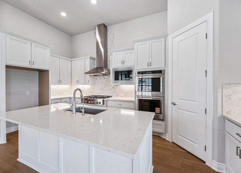 Kitchen with tasteful backsplash, white cabinets, stainless steel appliances, wall chimney exhaust hood, and recessed lighting