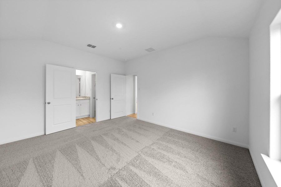 Unfurnished bedroom featuring vaulted ceiling, ensuite bathroom, light carpet, and recessed lighting