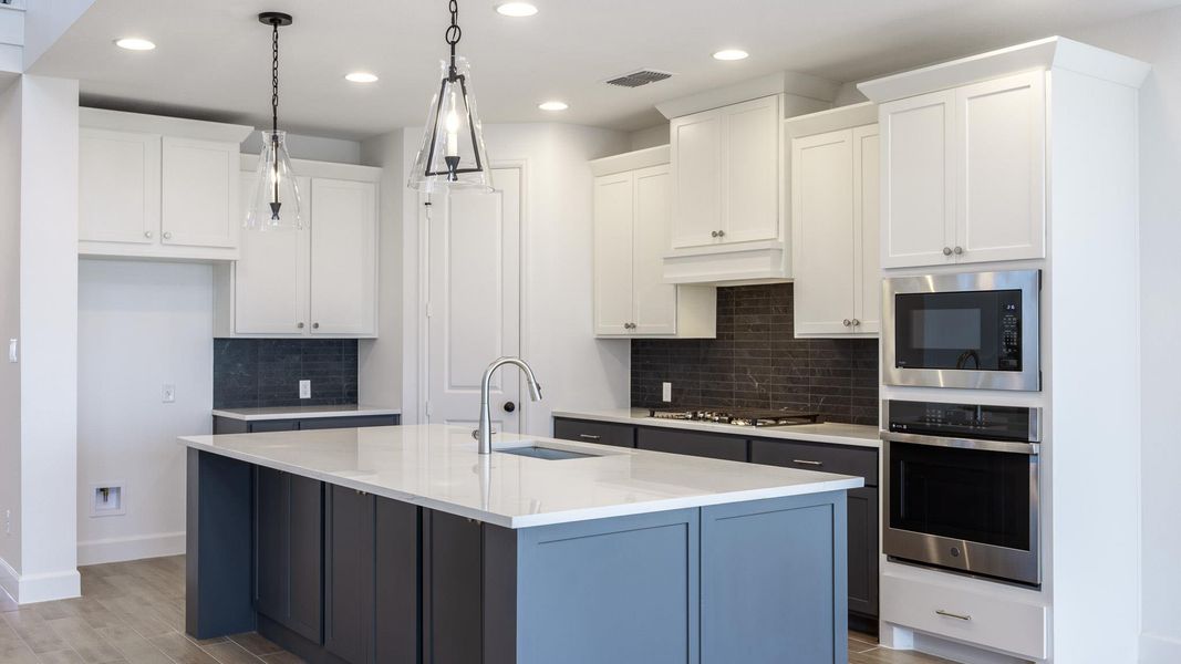 Kitchen with white cabinetry, backsplash, appliances with stainless steel finishes, an island with sink, and light wood finished floors Kitchen with white cabinetry, backsplash, appliances with stainless steel finishes, an island with sink, and light wood finished floors