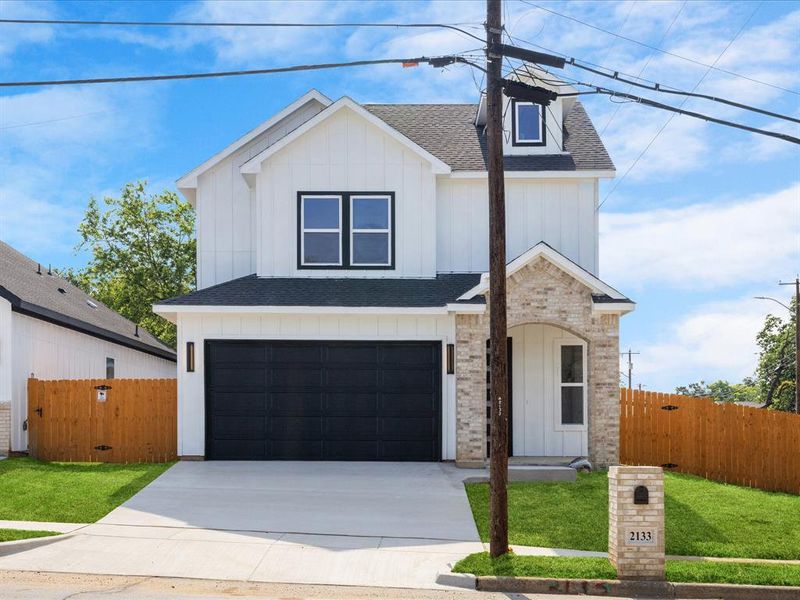 Contemporary two-story exterior featuring white board and batten siding, dark framed windows, an arched brick entry, an attached garage with a black door, and a matching brick mailbox Contemporary two-story exterior featuring white board and batten siding, dark framed windows, an arched brick entry, an attached garage with a black door, and a matching brick mailbox