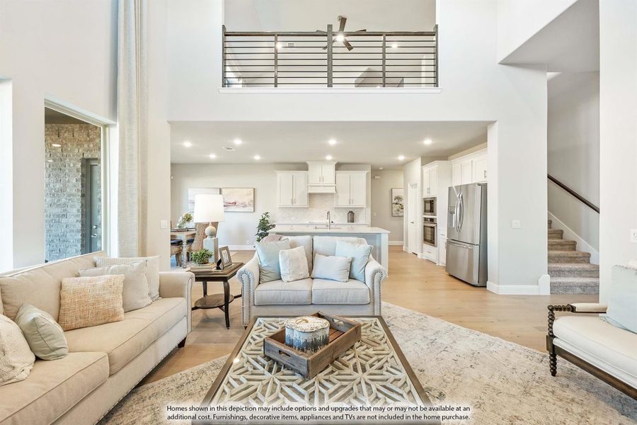 Open-concept living room with two-story ceiling, upper loft railing, and kitchen visible in background