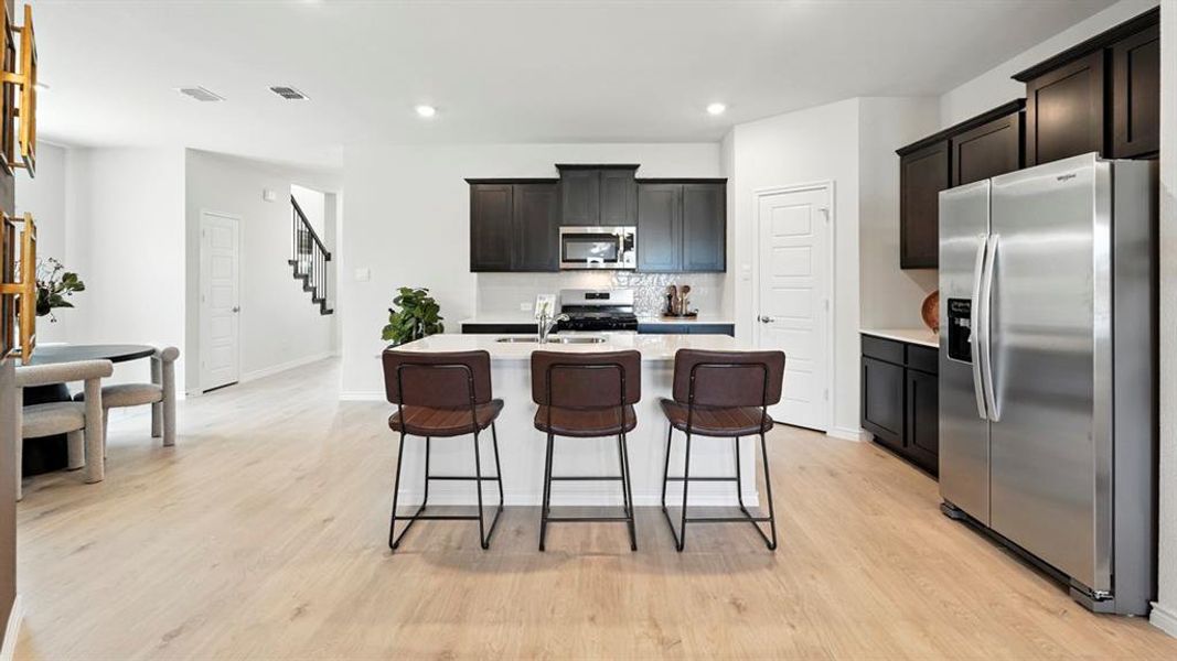 Kitchen featuring appliances with stainless steel finishes, tasteful backsplash, a center island with sink, light wood-type flooring, and a breakfast bar