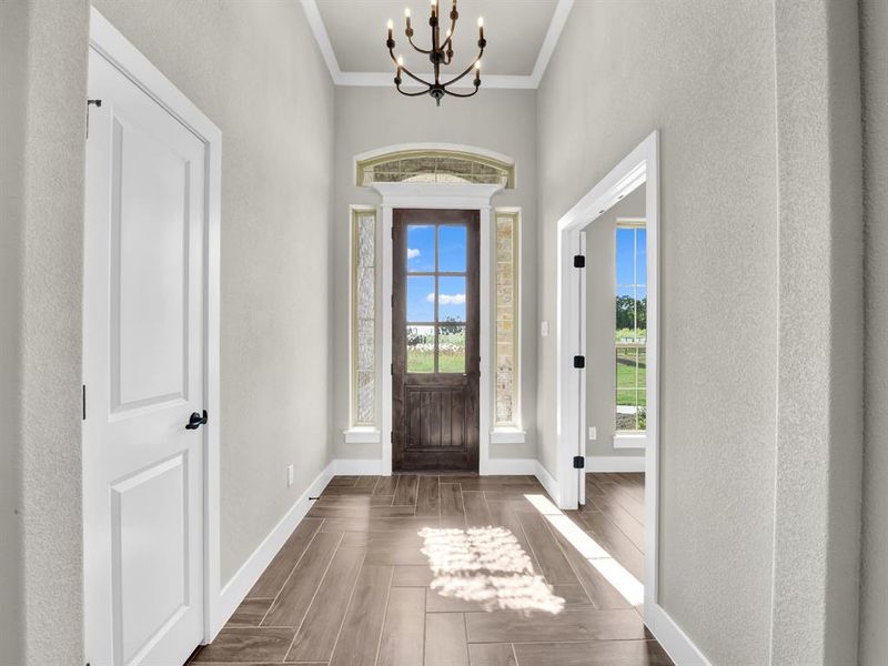 Foyer entrance featuring crown molding, a chandelier, parquet floors, and a textured wall Foyer entrance featuring crown molding, a chandelier, parquet floors, and a textured wall