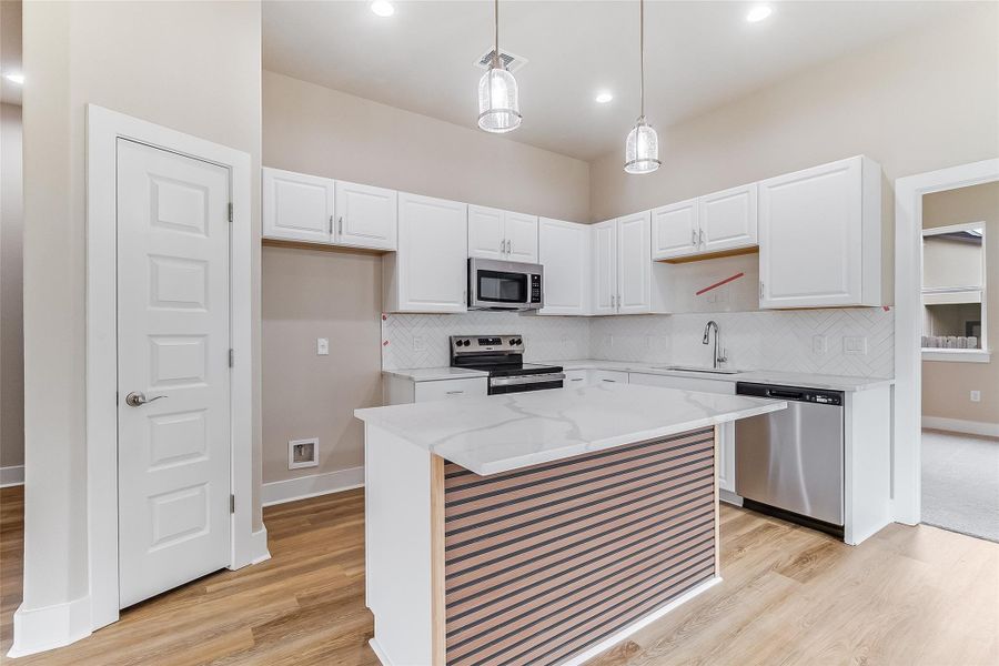 Kitchen with appliances with stainless steel finishes, light wood-style flooring, white cabinets, tasteful backsplash, and recessed lighting