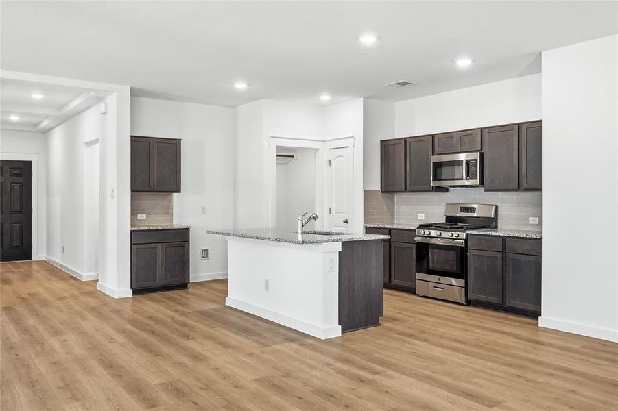 Kitchen with backsplash, stainless steel appliances, dark wood finish cabinetry, light stone counters, and recessed lighting