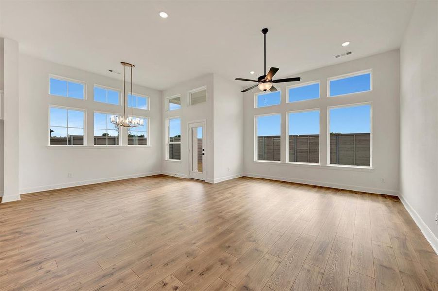 Expansive room featuring wood-finish flooring, numerous windows, high ceilings, a decorative chandelier, and a ceiling fan with integrated lighting