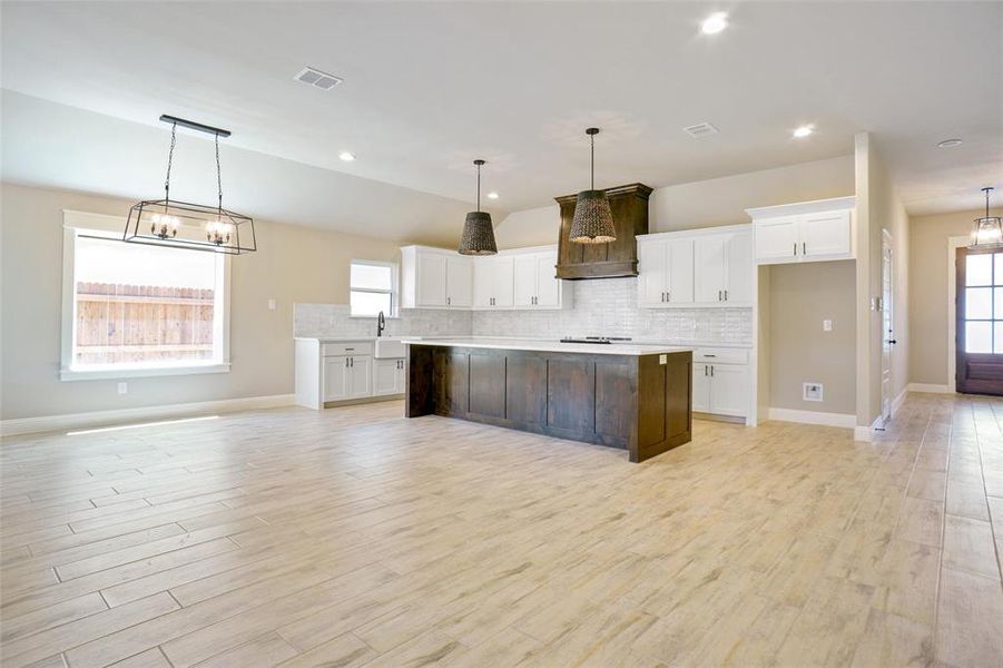 Kitchen with decorative light fixtures, white cabinetry, tasteful backsplash, a kitchen island, and light hardwood / wood-style floors