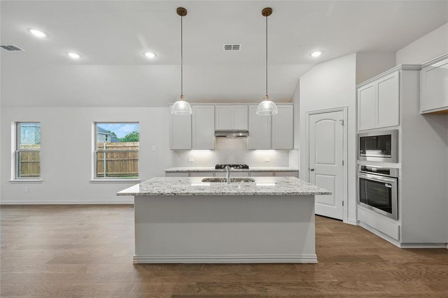Kitchen featuring lofted ceiling, a center island with sink, light stone countertops, stainless steel appliances, and white cabinets