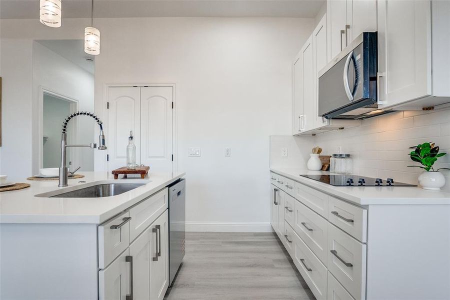 Kitchen featuring white cabinets, pendant lighting, light stone counters, backsplash, and light wood-type flooring Kitchen featuring white cabinets, pendant lighting, light stone counters, backsplash, and light wood-type flooring