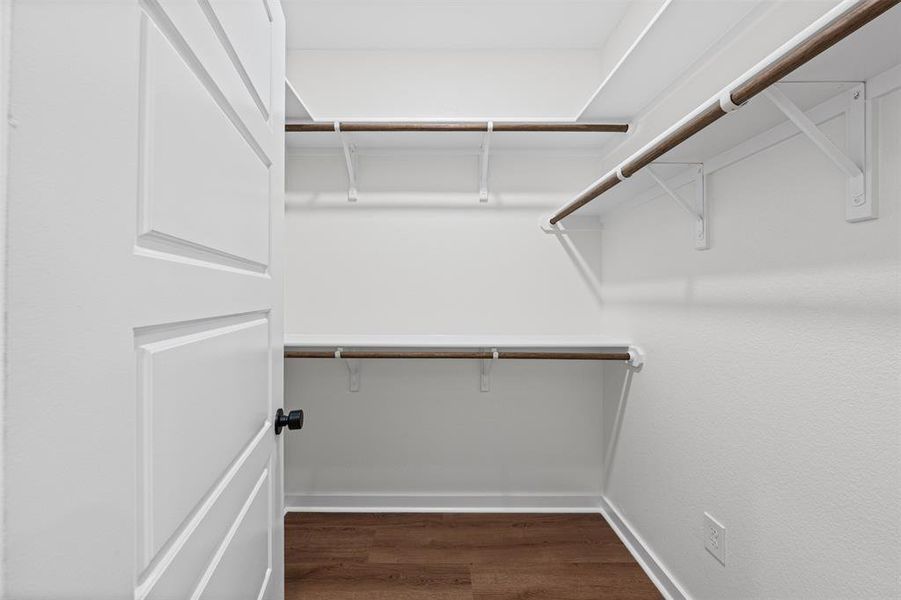 Well-appointed closet featuring white shelving with hanging rods and durable wood flooring