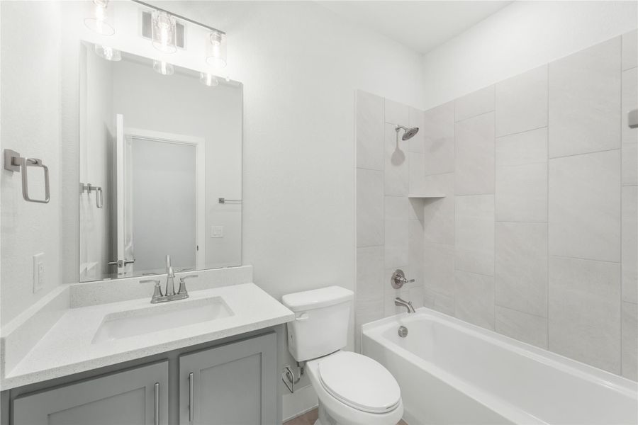 Bathroom with gray vanity, white quartz countertop, and tiled shower-tub combo with built-in niche