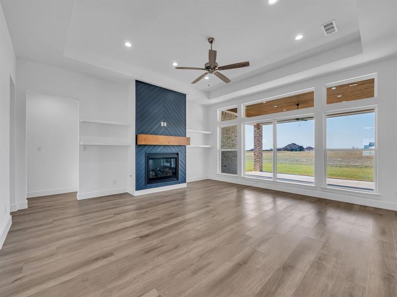 Unfurnished living room with light hardwood / wood-style flooring, a large fireplace, a raised ceiling, and built in shelves