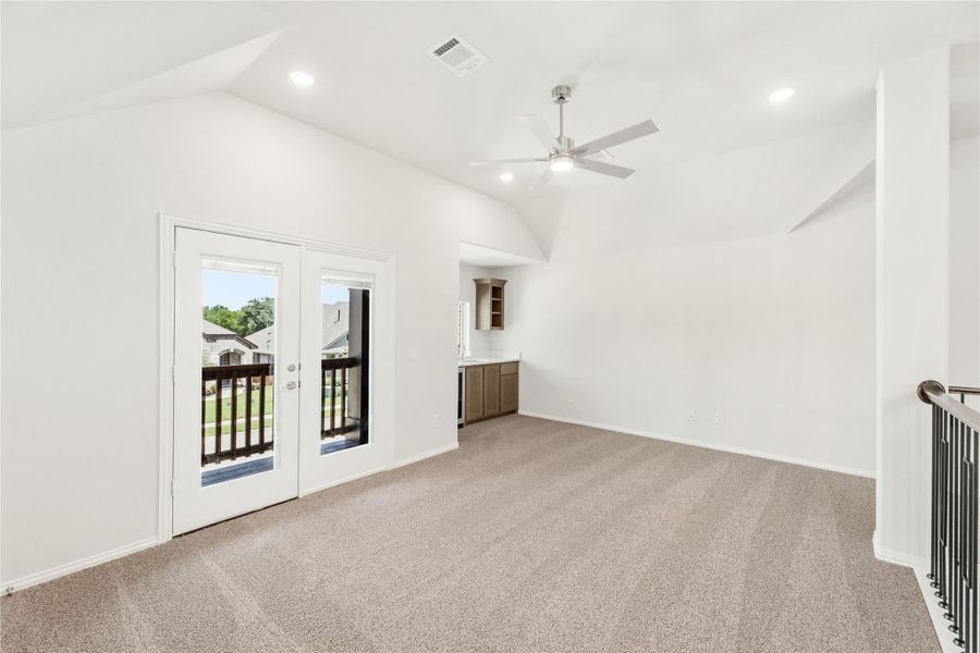 Open bonus room with vaulted ceiling, ceiling fan, carpet, French doors to balcony, and wet bar area