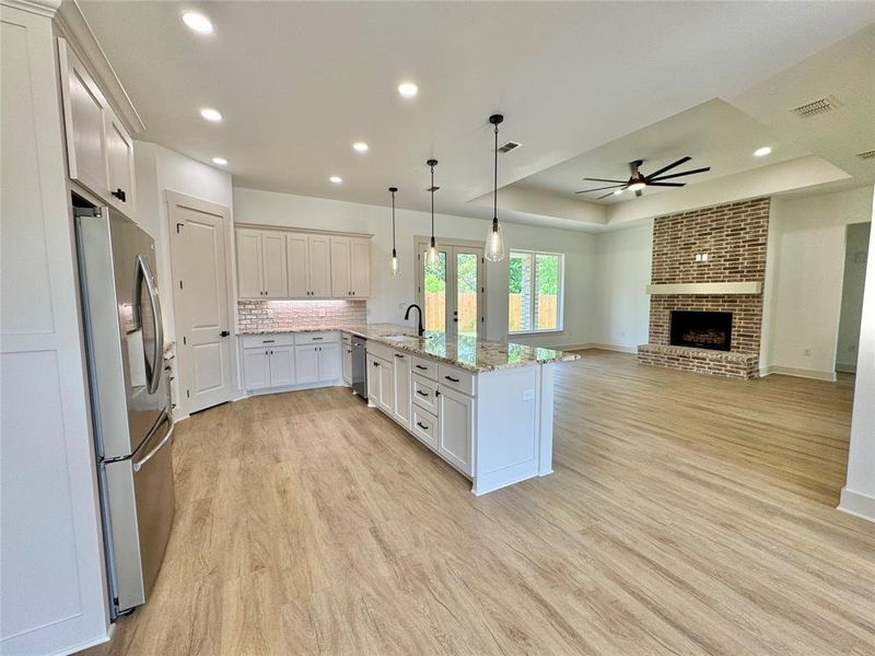 Kitchen with a tray ceiling, decorative light fixtures, tasteful backsplash, light stone countertops, and light wood-style floors