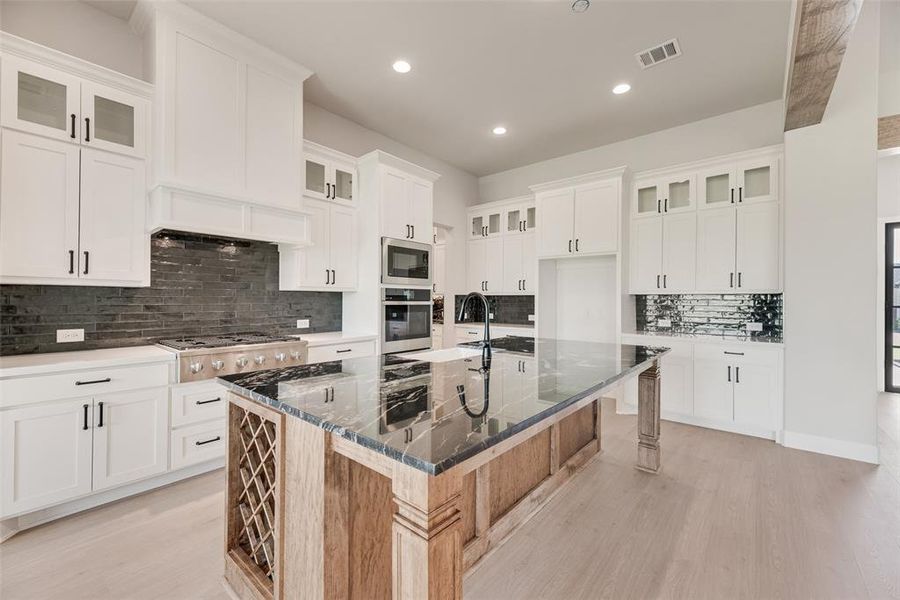 Kitchen featuring glass insert cabinets, decorative backsplash, a large island, dark stone countertops, and white cabinets